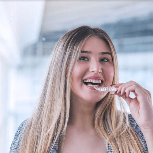 young woman putting in her clear braces whilst smiling towards the camera.